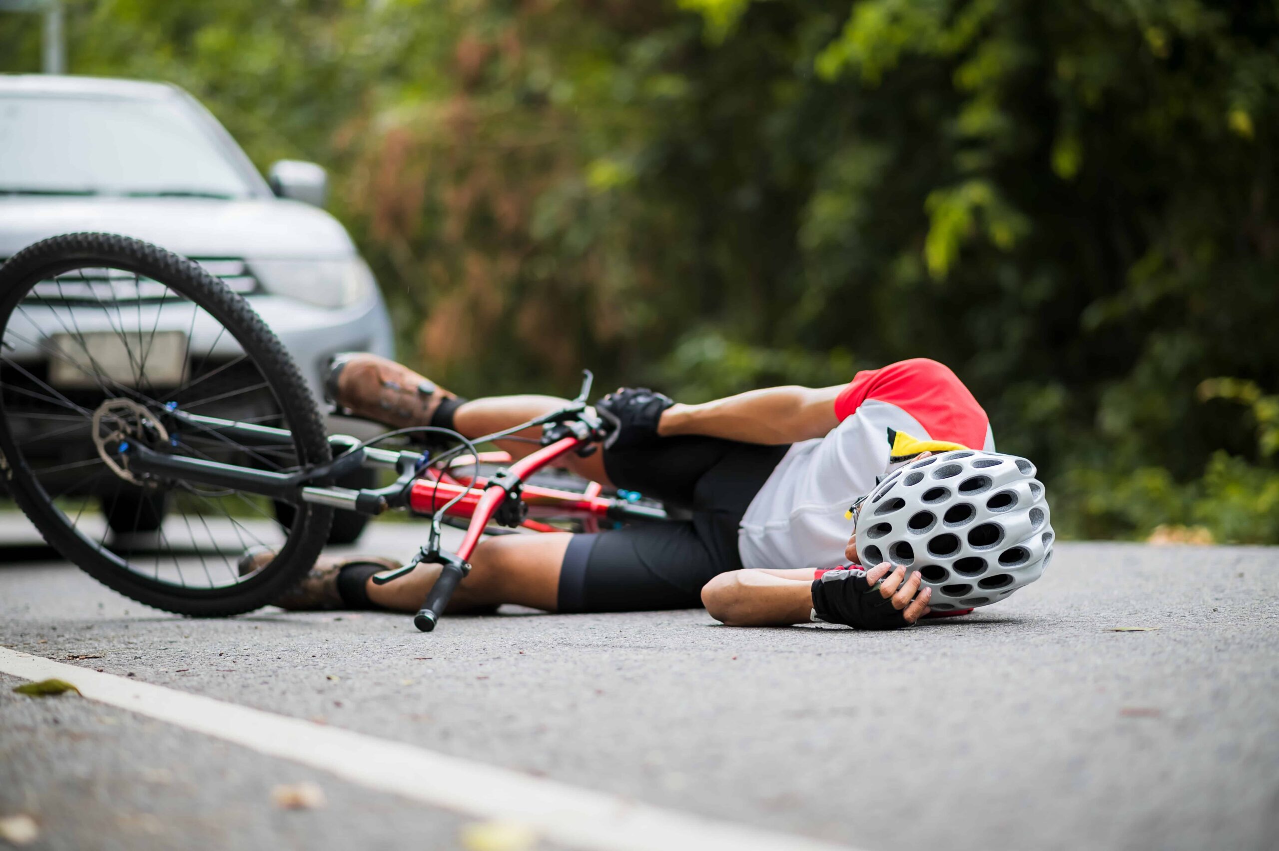 Injured cyclist lying on the road next to a bicycle after a collision with a car, representing a bicycle accident and road safety incident.