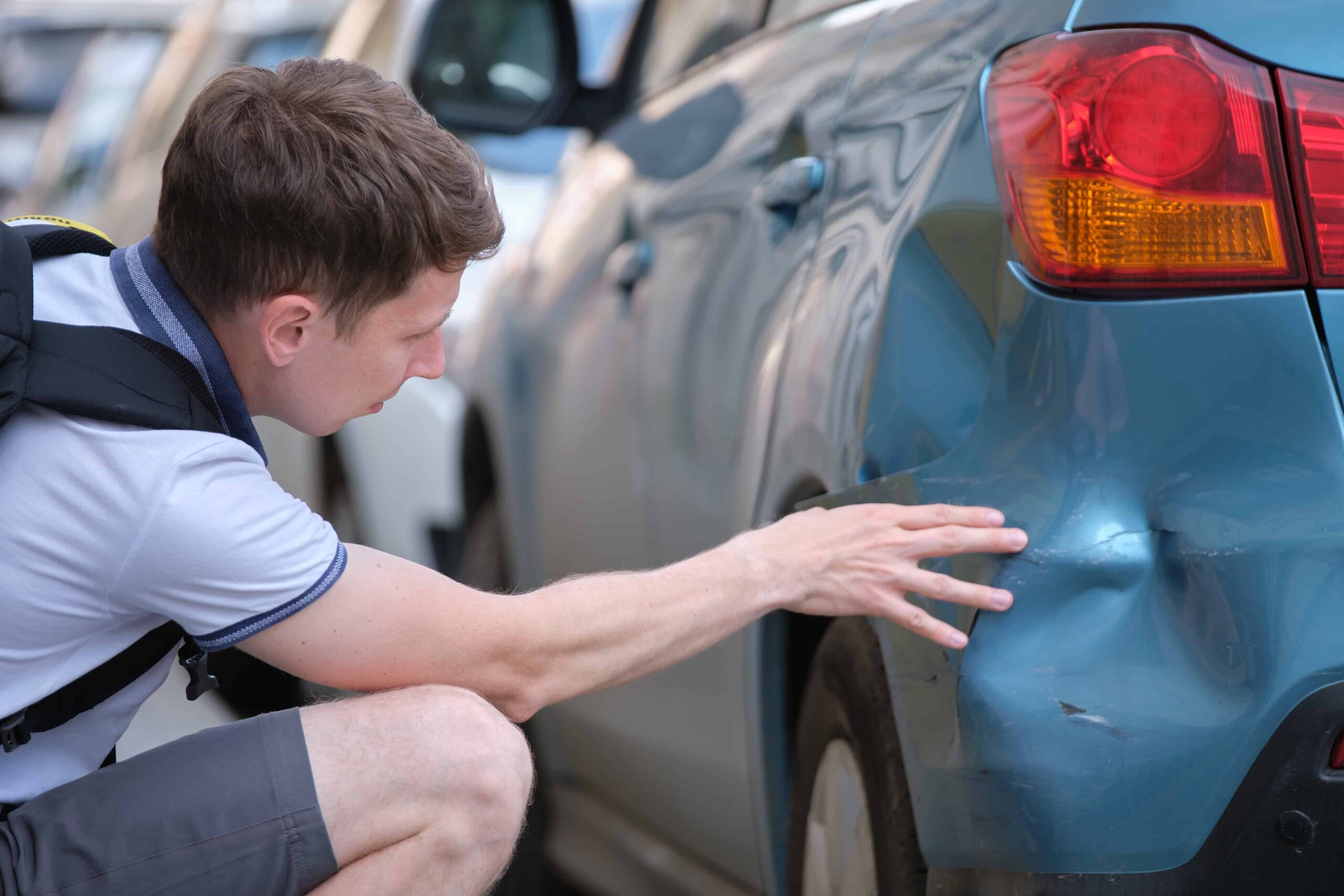 Man inspecting damage to a car bumper after a minor traffic accident, assessing vehicle collision damage