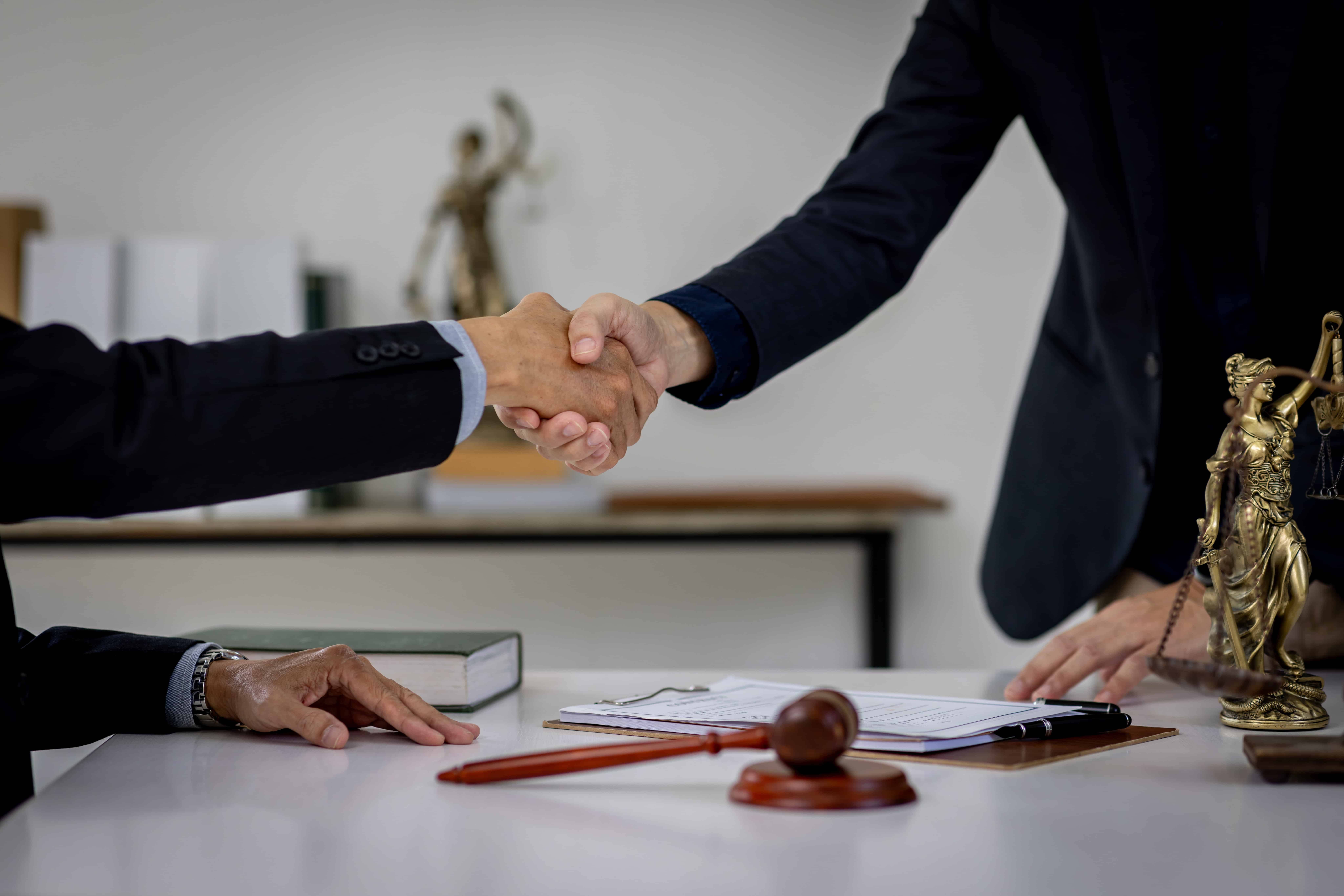 Attorneys shaking hands over a signed contract with a judge’s gavel on the desk, symbolizing a legal agreement or settlement.