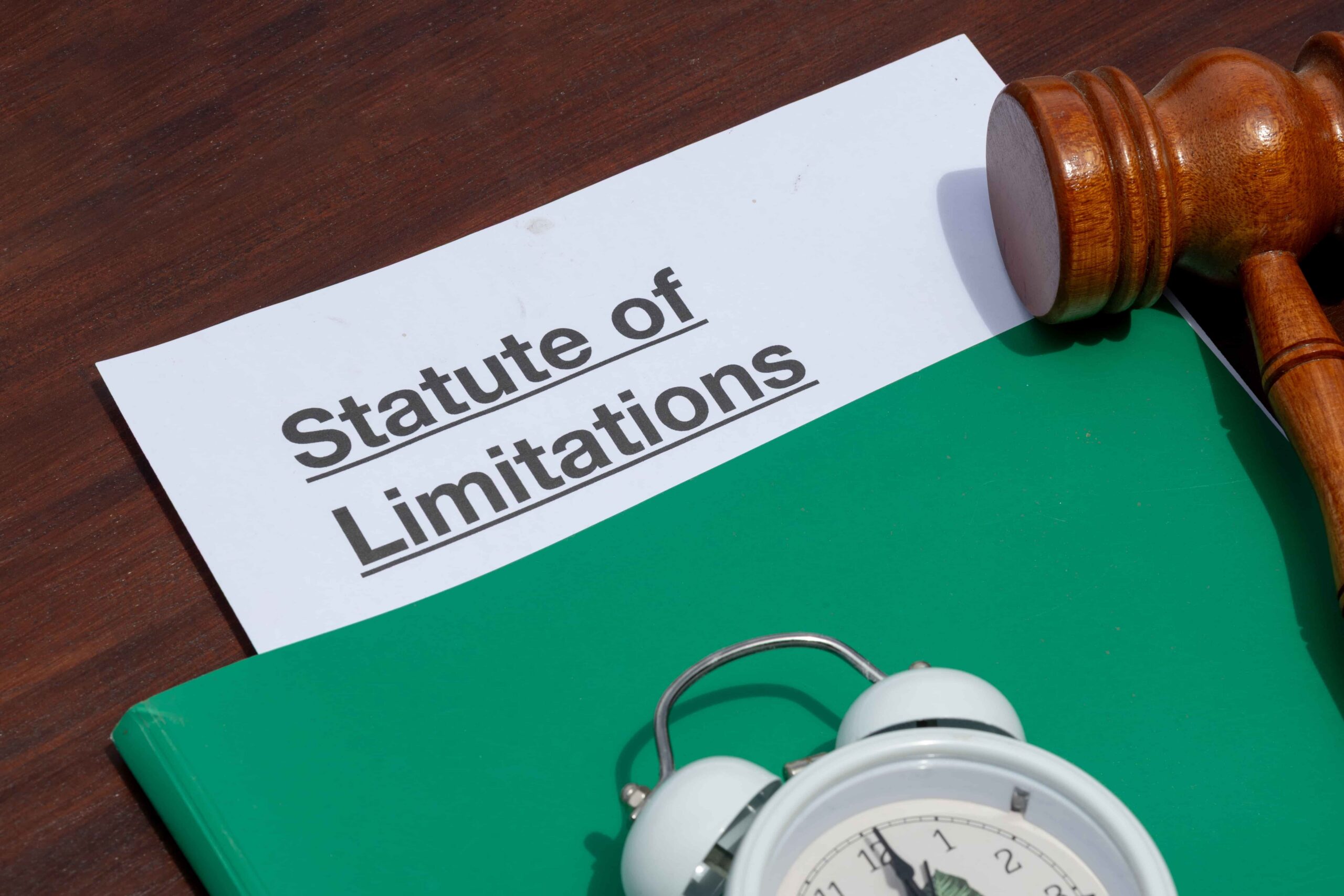 Statute of limitations document with gavel and alarm clock on desk, symbolizing legal time limits.