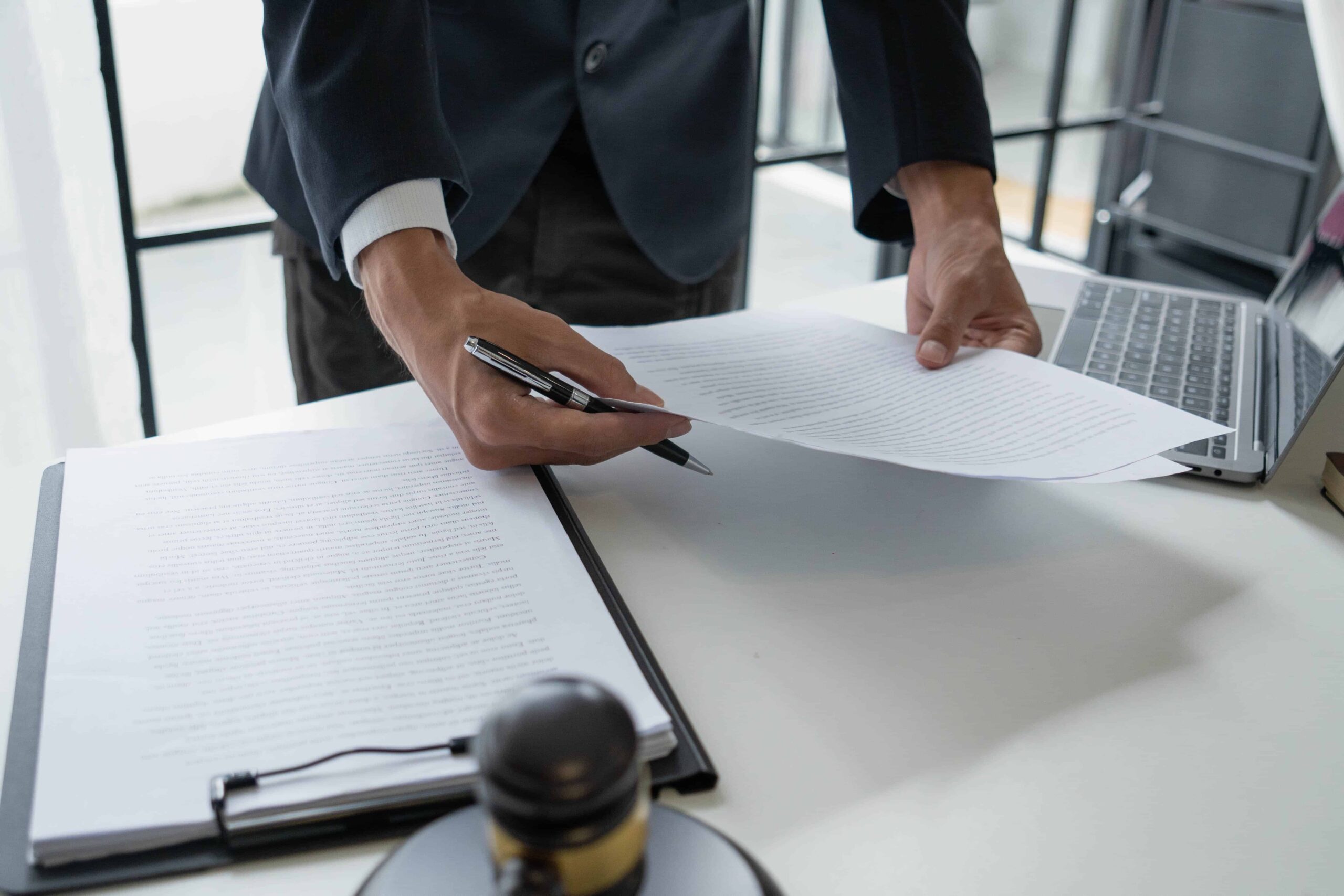 Attorney reviewing and signing legal documents at a desk with gavel and laptop.